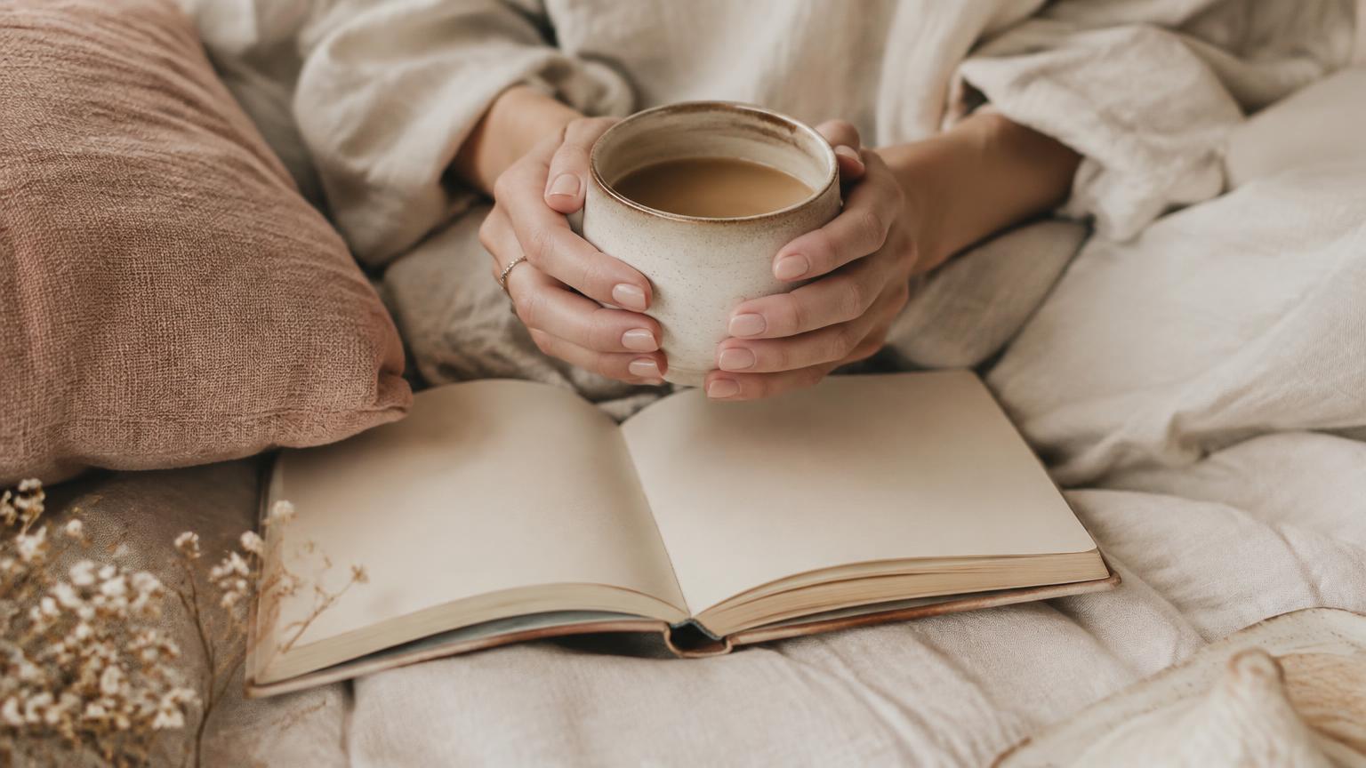 Hands holding a warm cup over an open journal on linen